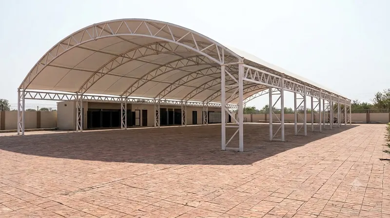 Long arched clear-span tensile roof over an open paved yard